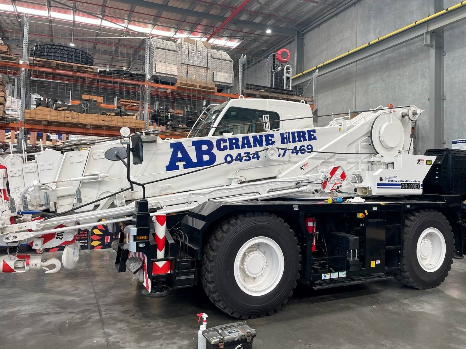 White AB Crane Hire mobile crane inside a warehouse, with large wheels and a raised boom.