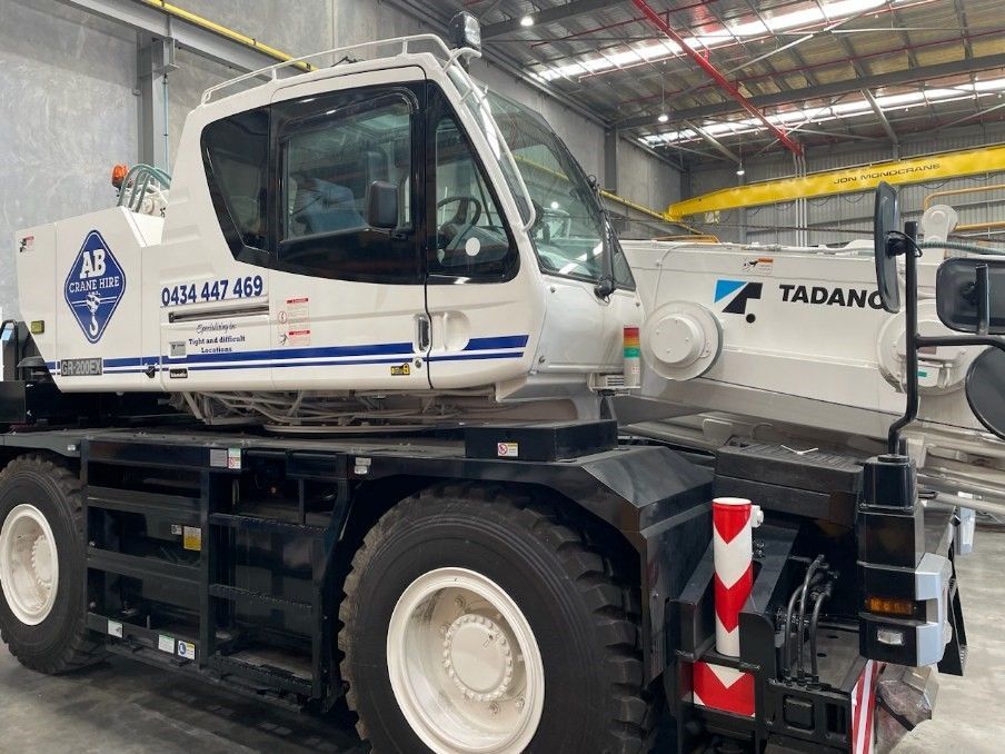 Gray Tadano mobile crane indoors, side view on black chassis with white cab and red-striped outriggers