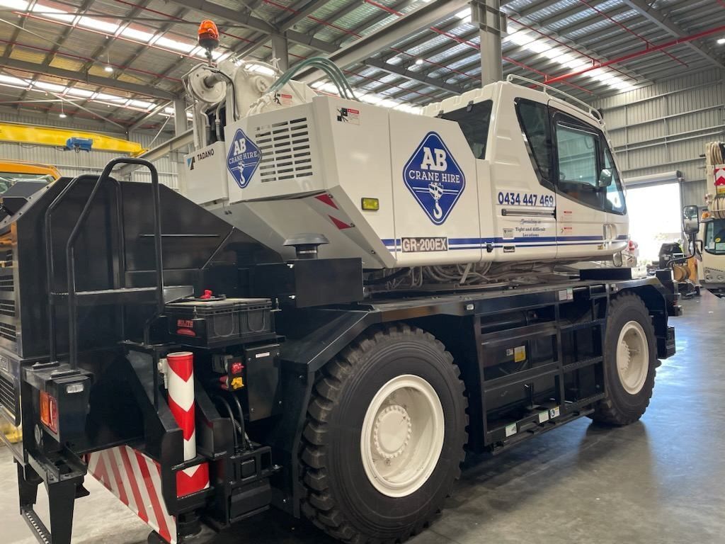 White and black mobile crane in a warehouse, side view, with large tires and red-white safety markings