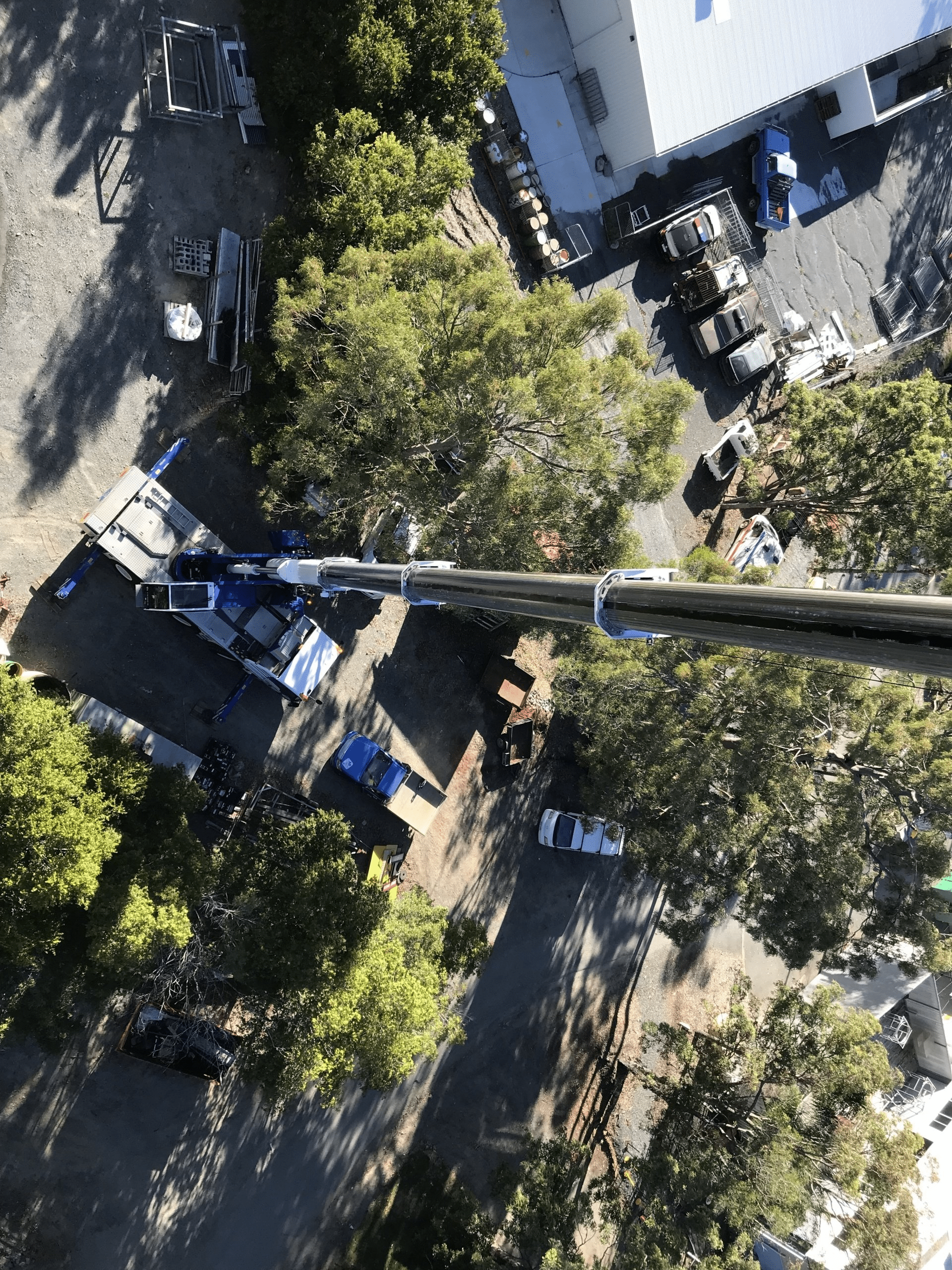 Aerial view of a tree-lined street with parked cars and a long utility pole crossing the scene.