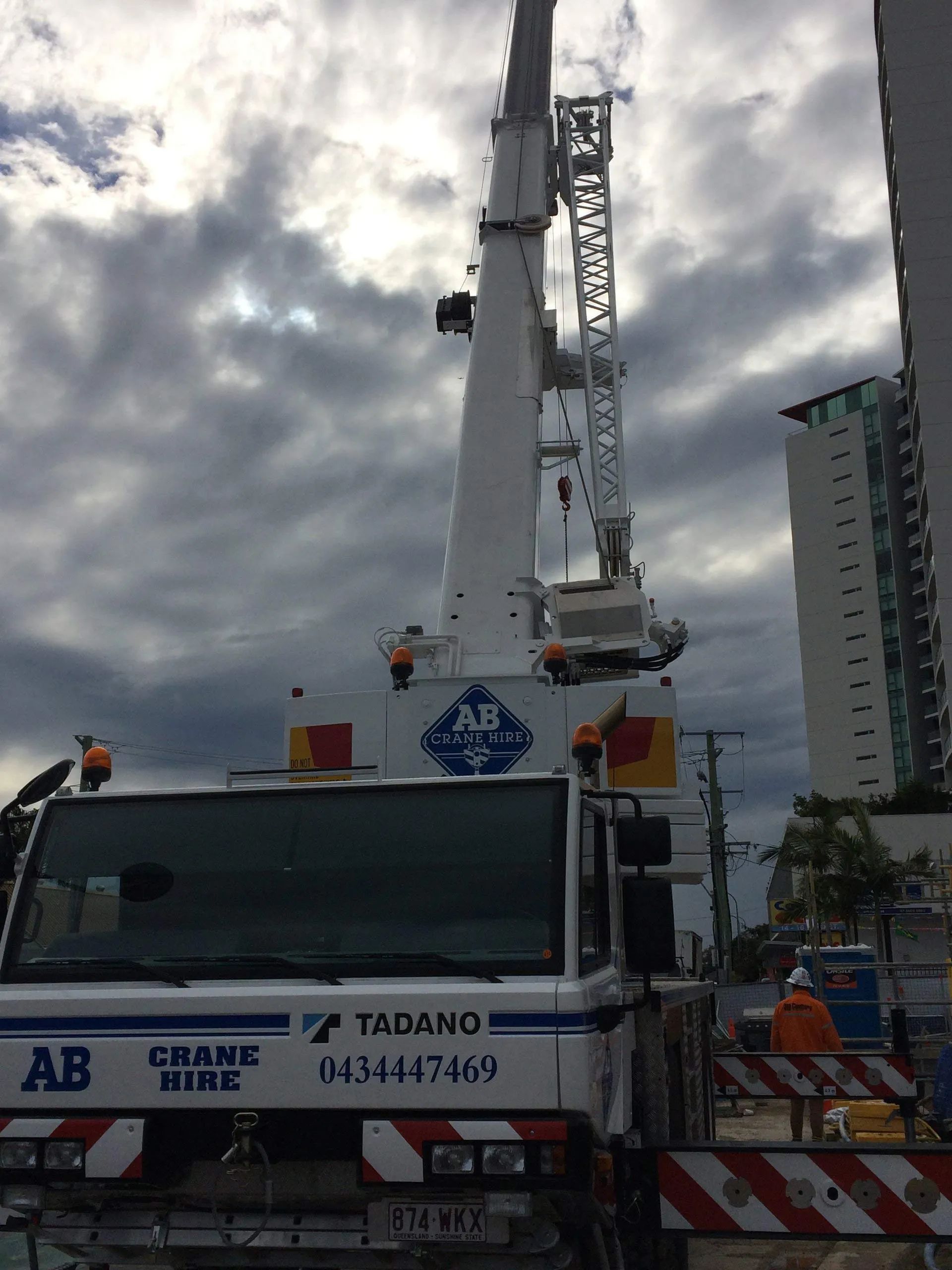 Crane truck lifting a heavy load at a construction site under a cloudy sky