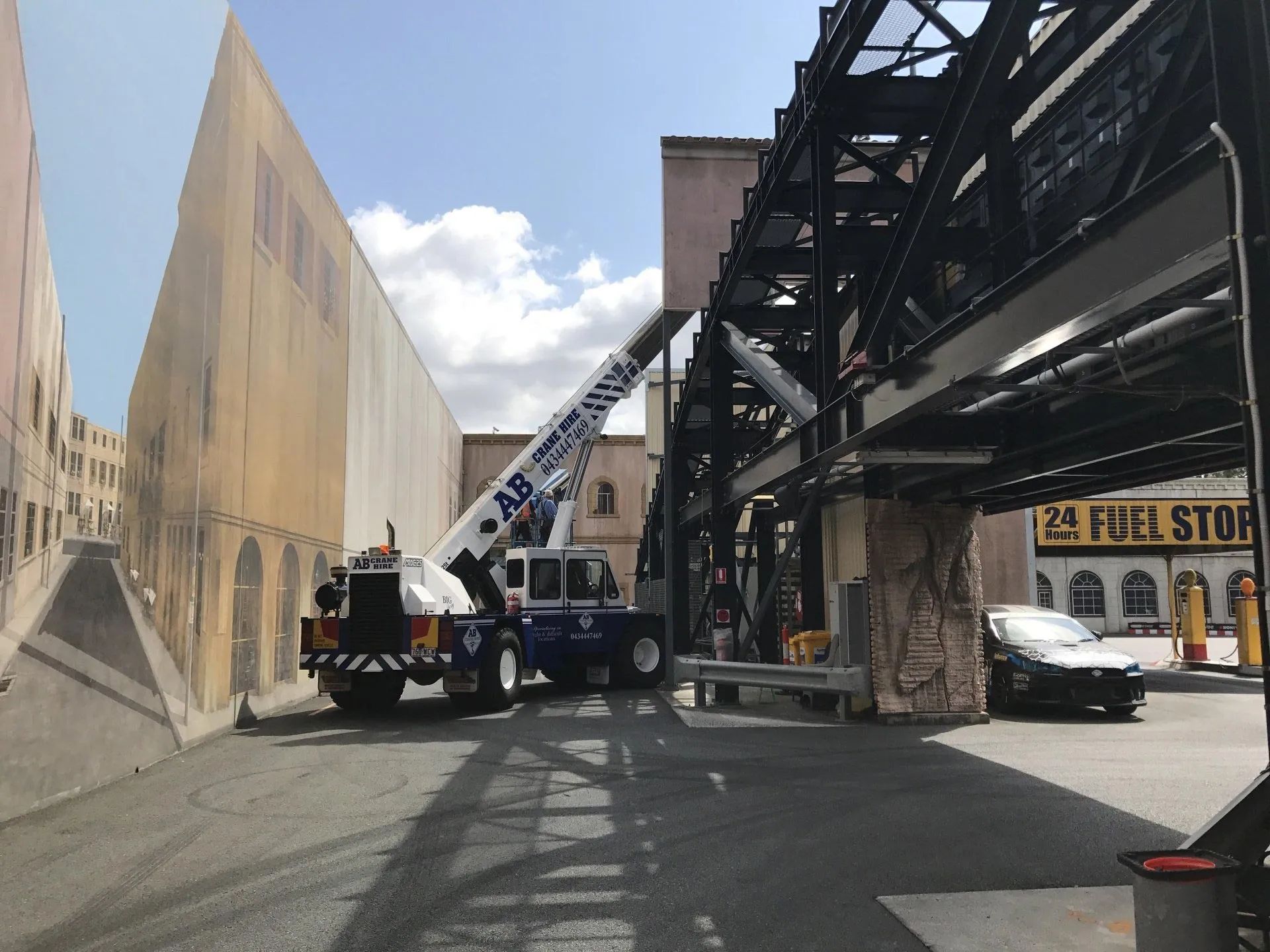Tow truck lifting a railcar on a city street beside an elevated track, with storefronts nearby