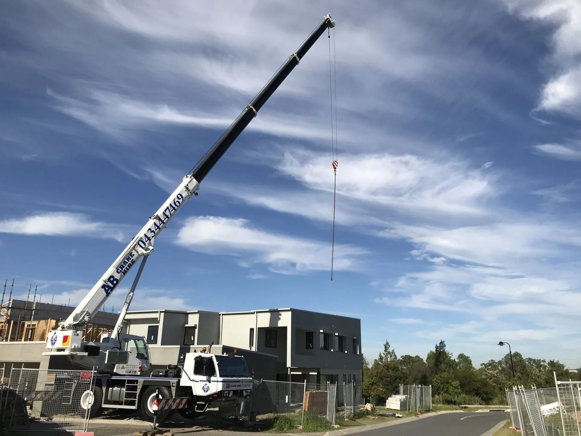 Crane lifting materials at a construction site beside a partly built house under a blue sky