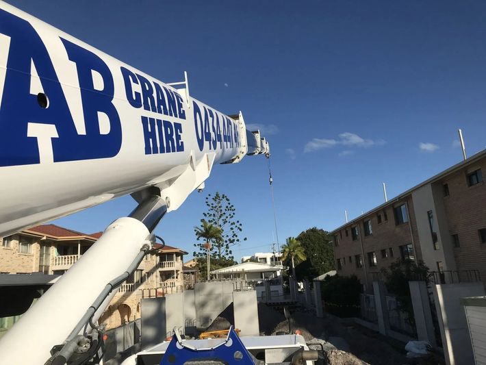 White crane arm with blue lettering over a sunny residential street and apartment buildings