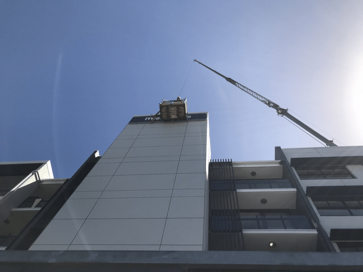 Tall building under construction against a blue sky, with a crane on the right.