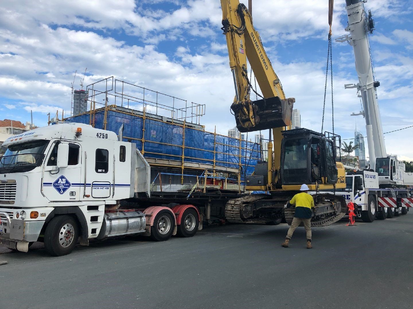 Crane lifting a blue-wrapped load onto a flatbed truck at a construction site