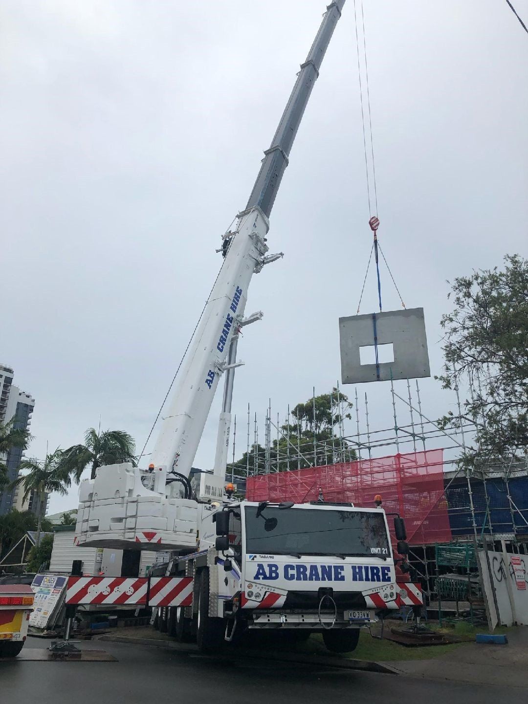 Mobile crane lifting a concrete block on a truck at a construction site
