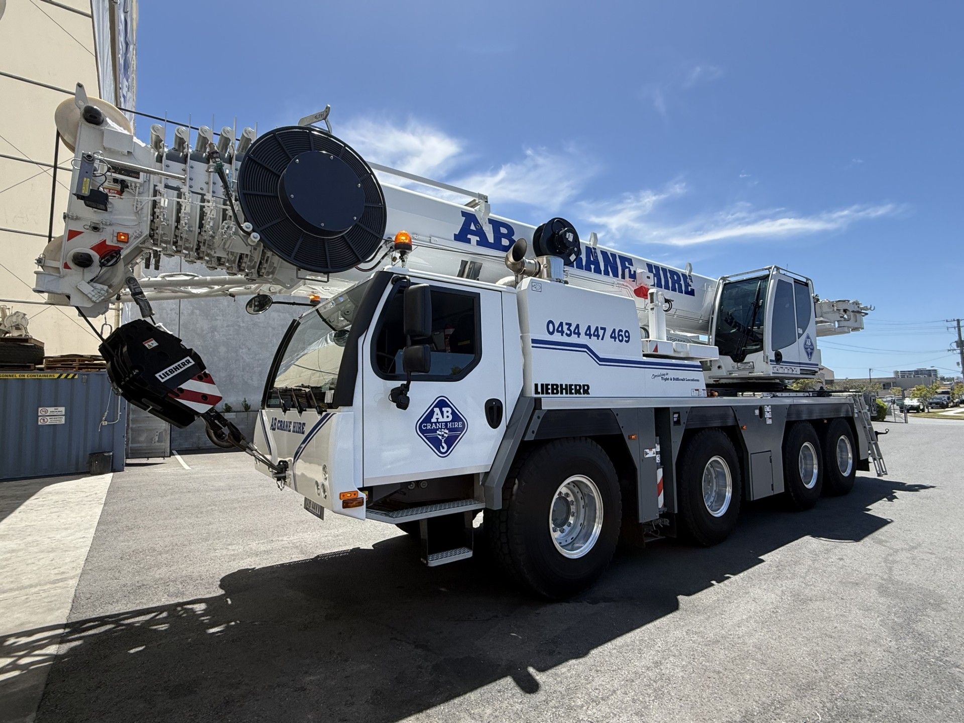 White mobile crane truck on a road under a blue sky, with a raised boom and large tires