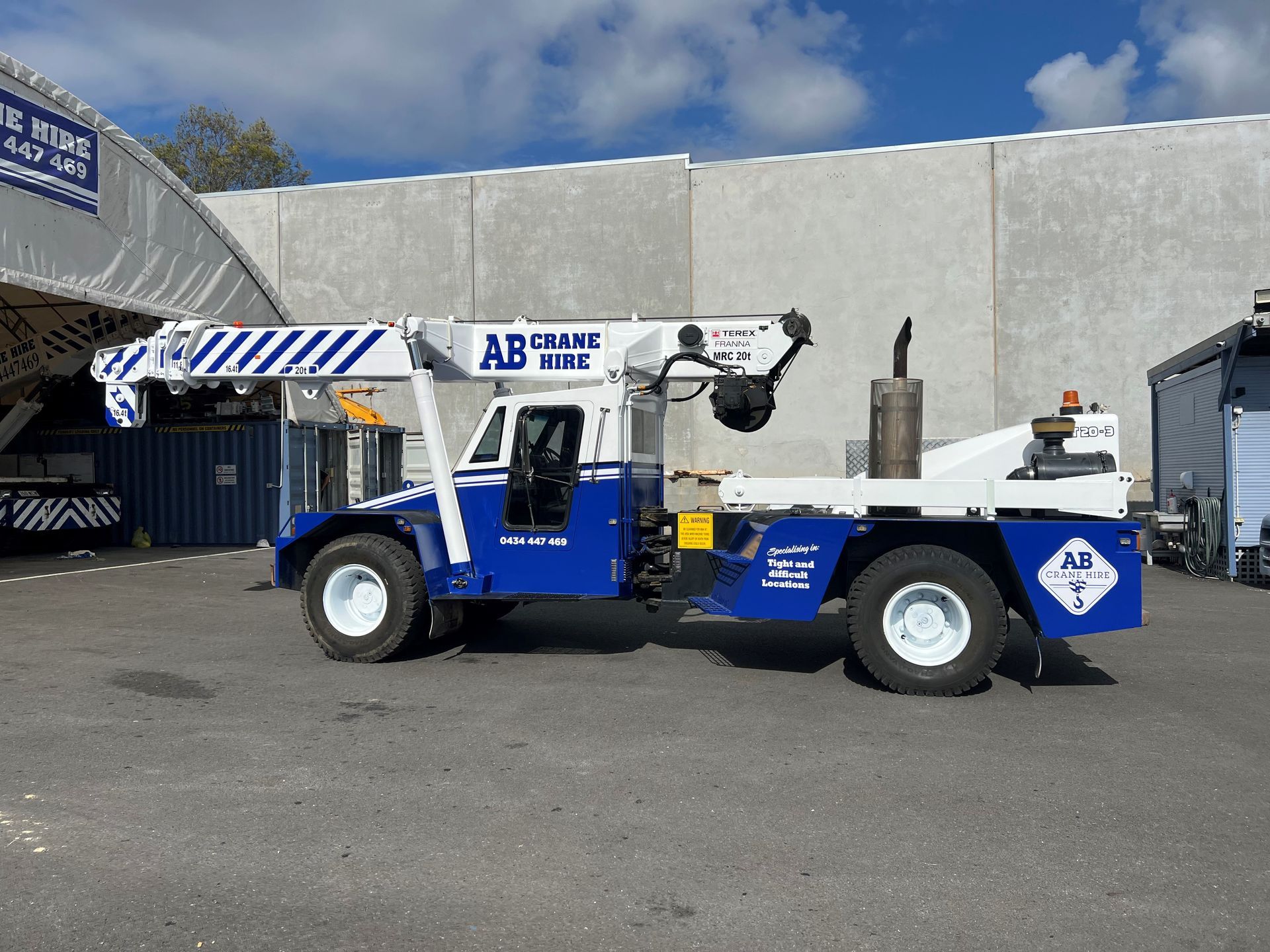Blue industrial utility vehicle parked outside a building with “AB Crane” signage.