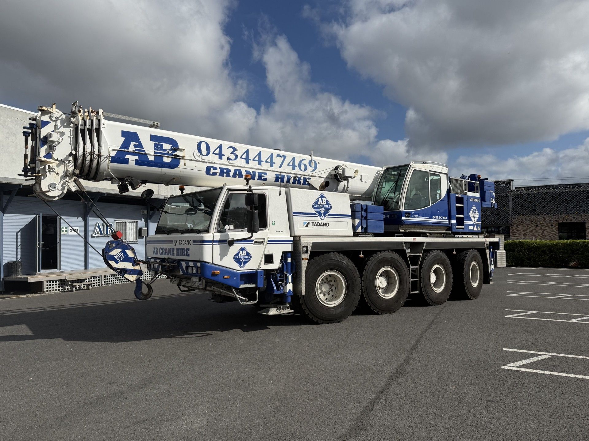Blue-and-white crane truck parked on asphalt under cloudy sky