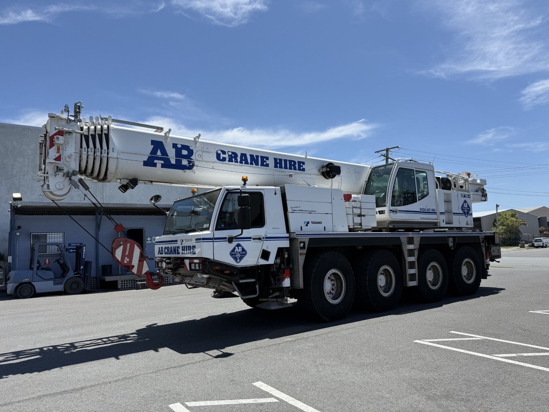 White AB crane truck parked in a lot under a blue sky
