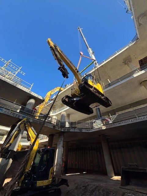 Yellow excavator hanging from a crane at a construction site under a blue sky