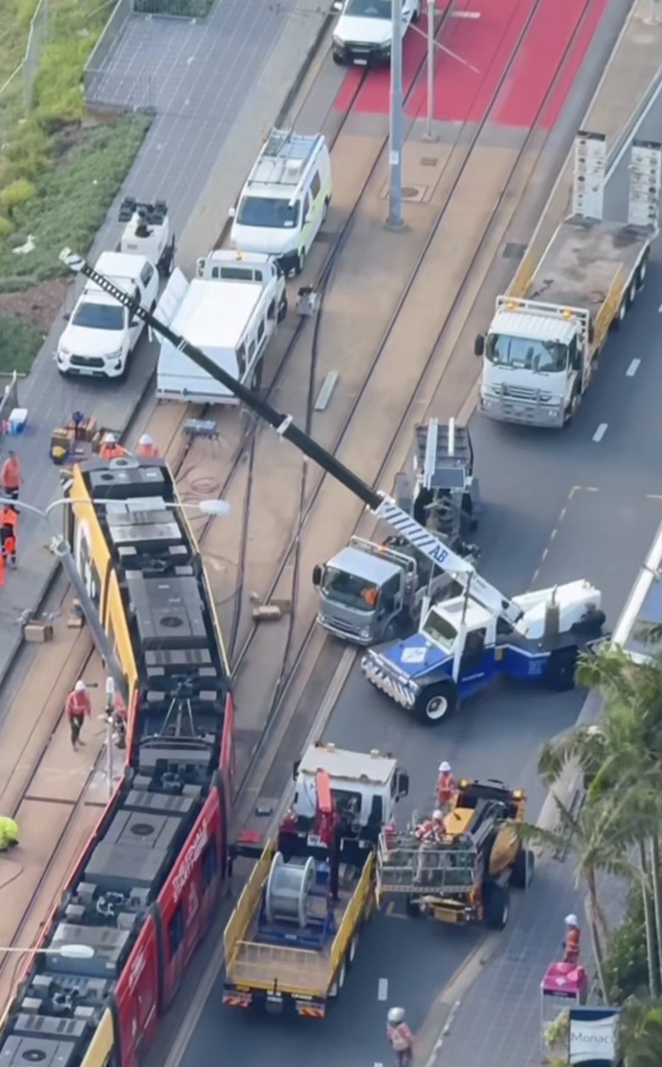 Aerial view of a road crash with tow trucks, a tipped-over vehicle, and workers near a red bus.