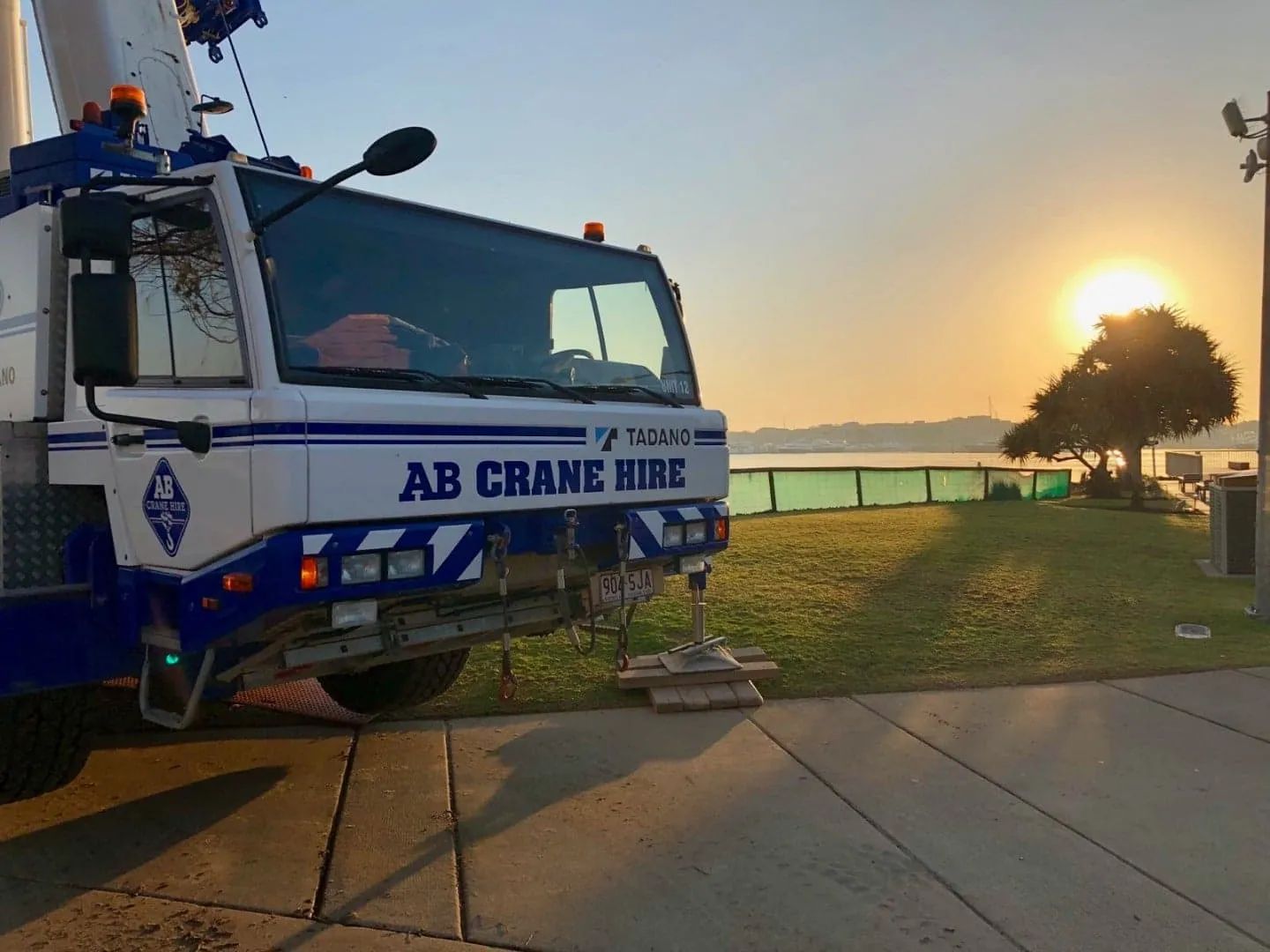 AB Crane Hire truck parked by a waterfront at sunset