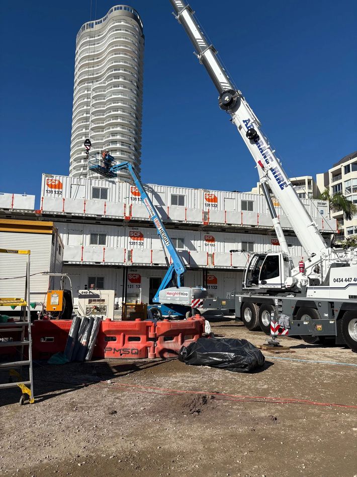 Construction site with cranes and a tall high-rise wrapped in scaffolding under a clear blue sky