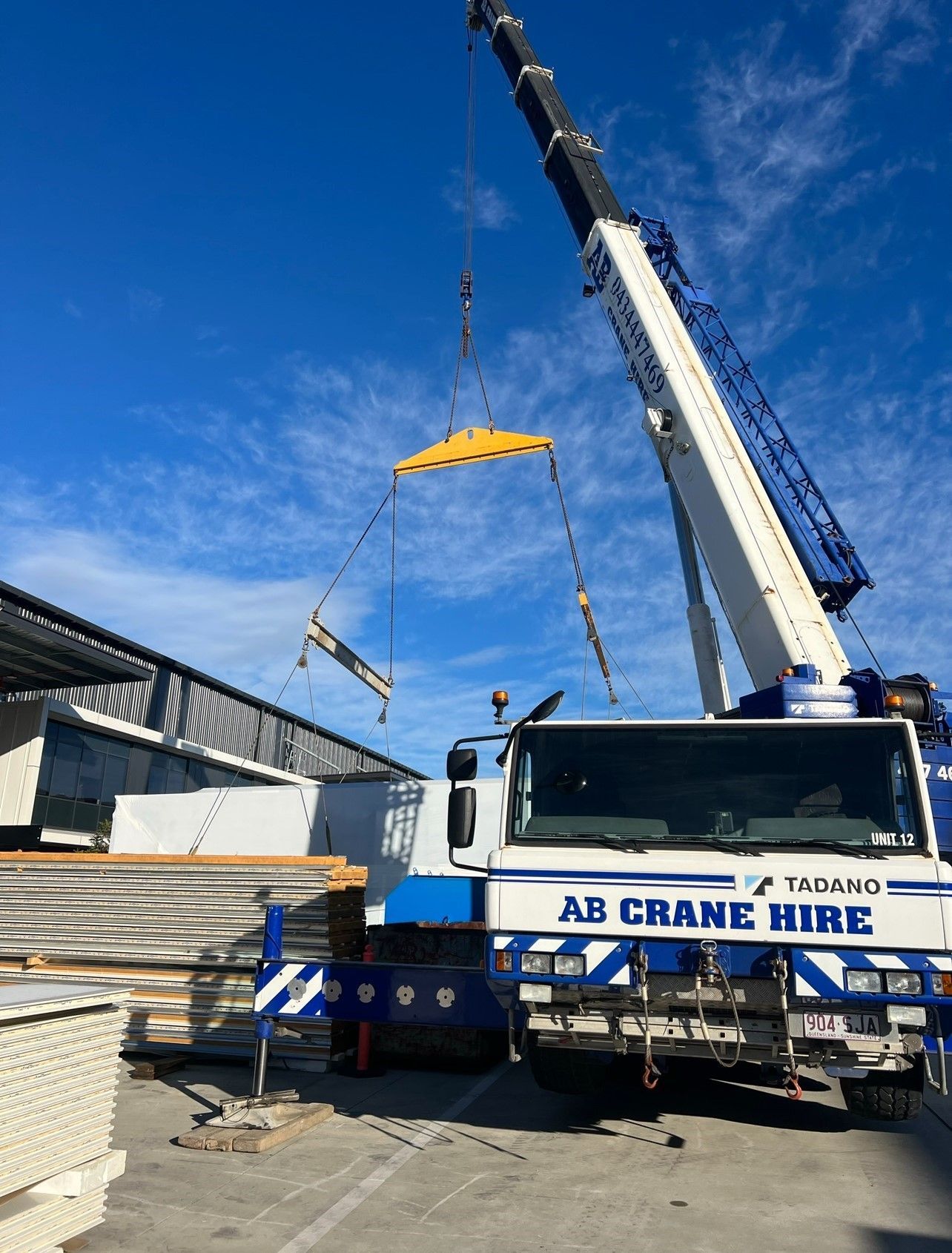 White AB Crane Hire crane lifting materials at a construction site under a blue sky