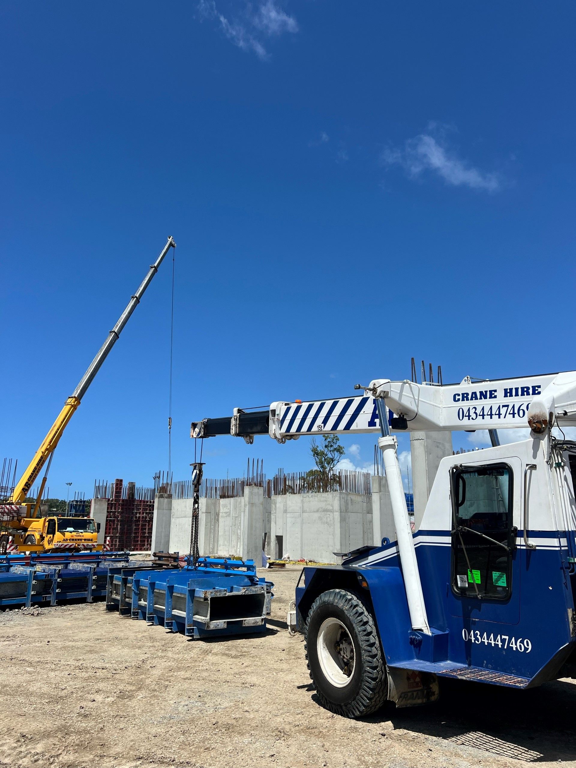 Blue-and-white crane truck at a construction site under a clear blue sky