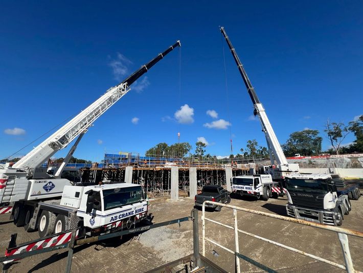 Construction site with two white cranes lifting over a partially built concrete structure under a blue sky