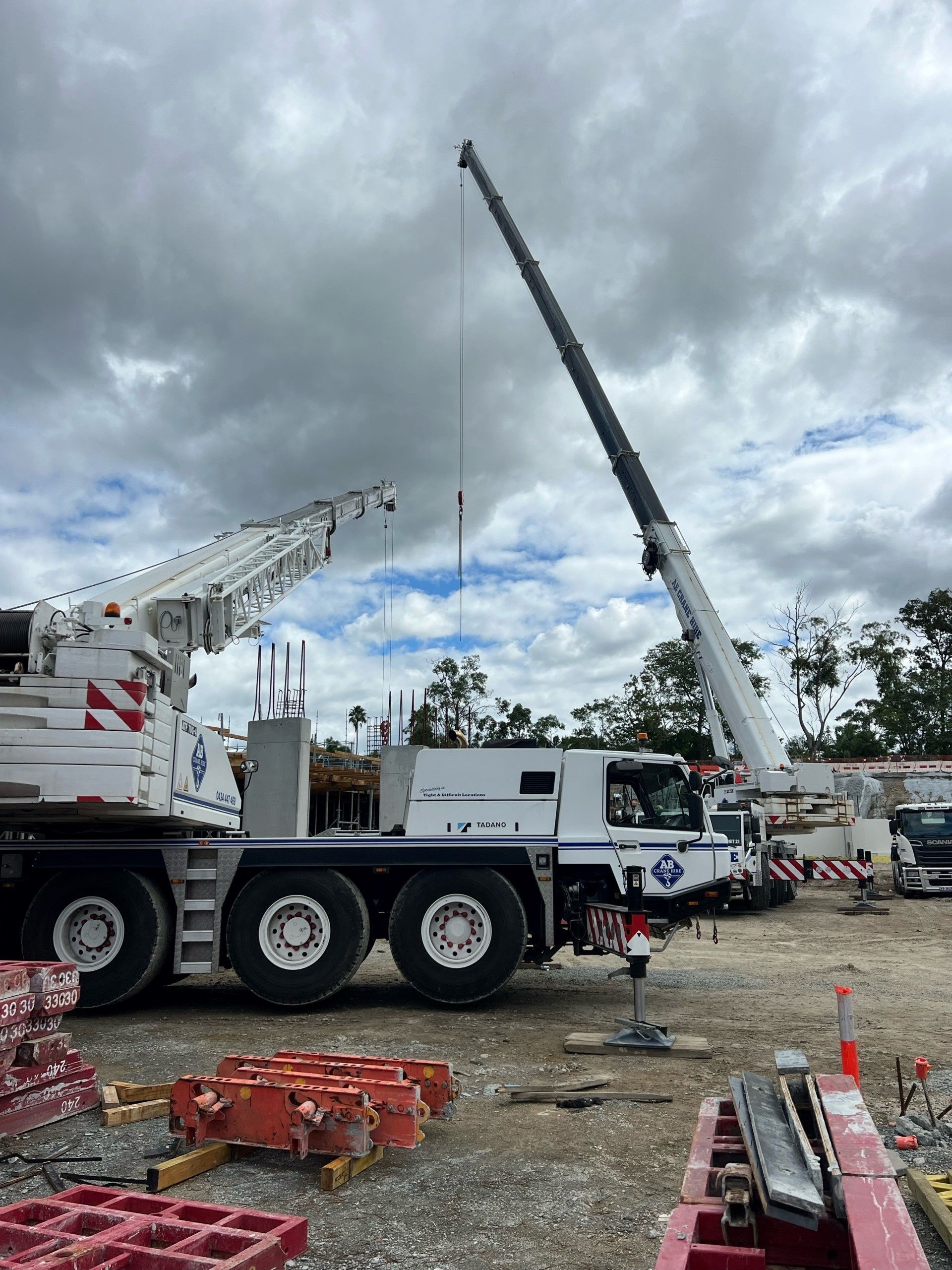 Two large cranes at a work site under cloudy skies, with equipment and trucks nearby