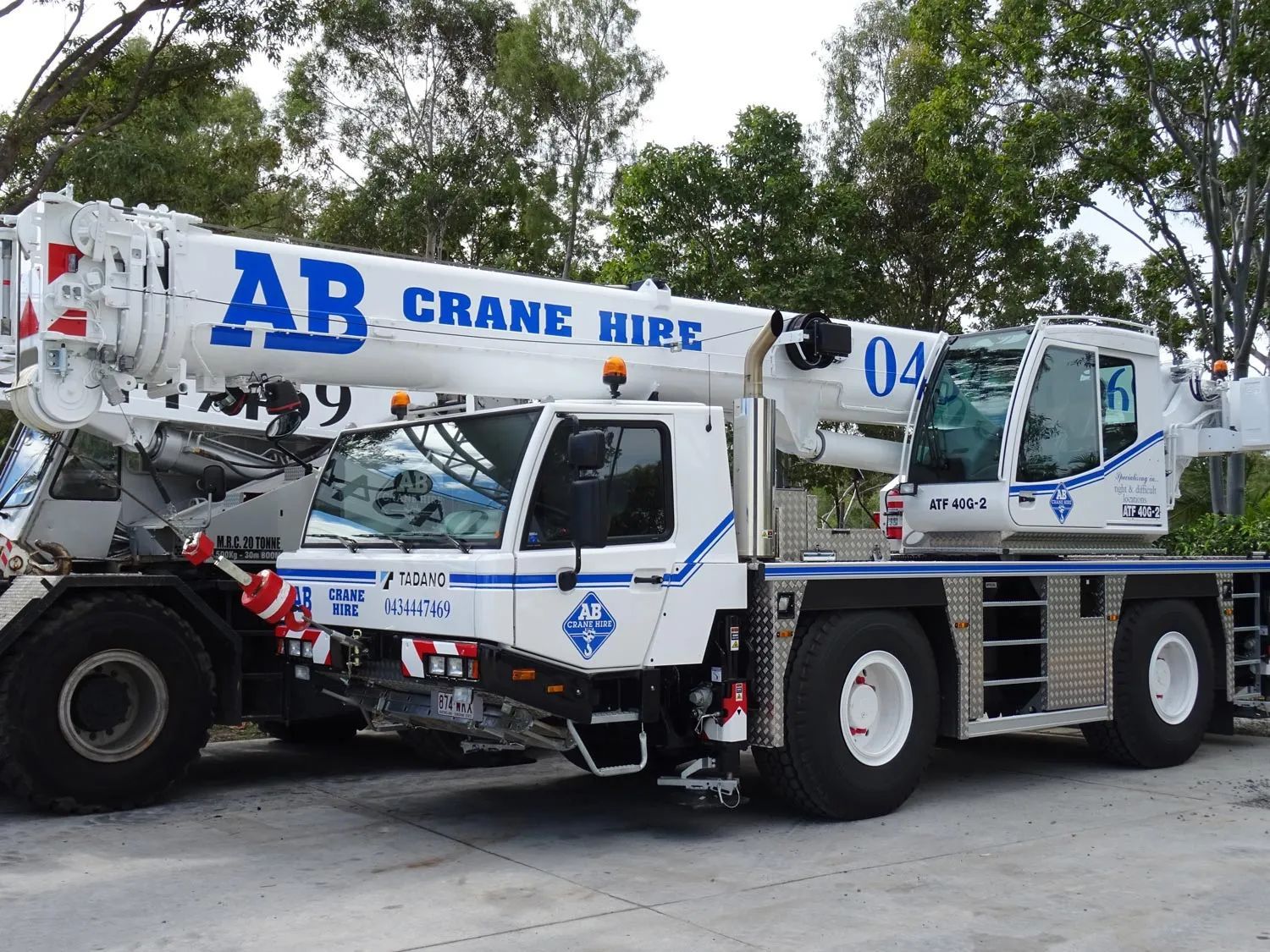 White crane truck with blue “AB Crane Hire” lettering parked outdoors on a road.