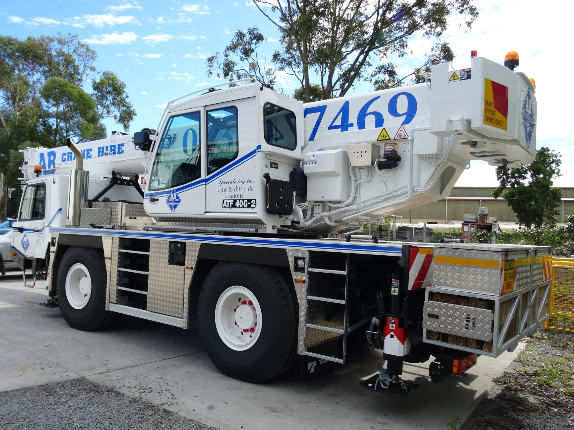 White utility truck with mounted boom lift, numbered 7469, parked on a roadside under trees.