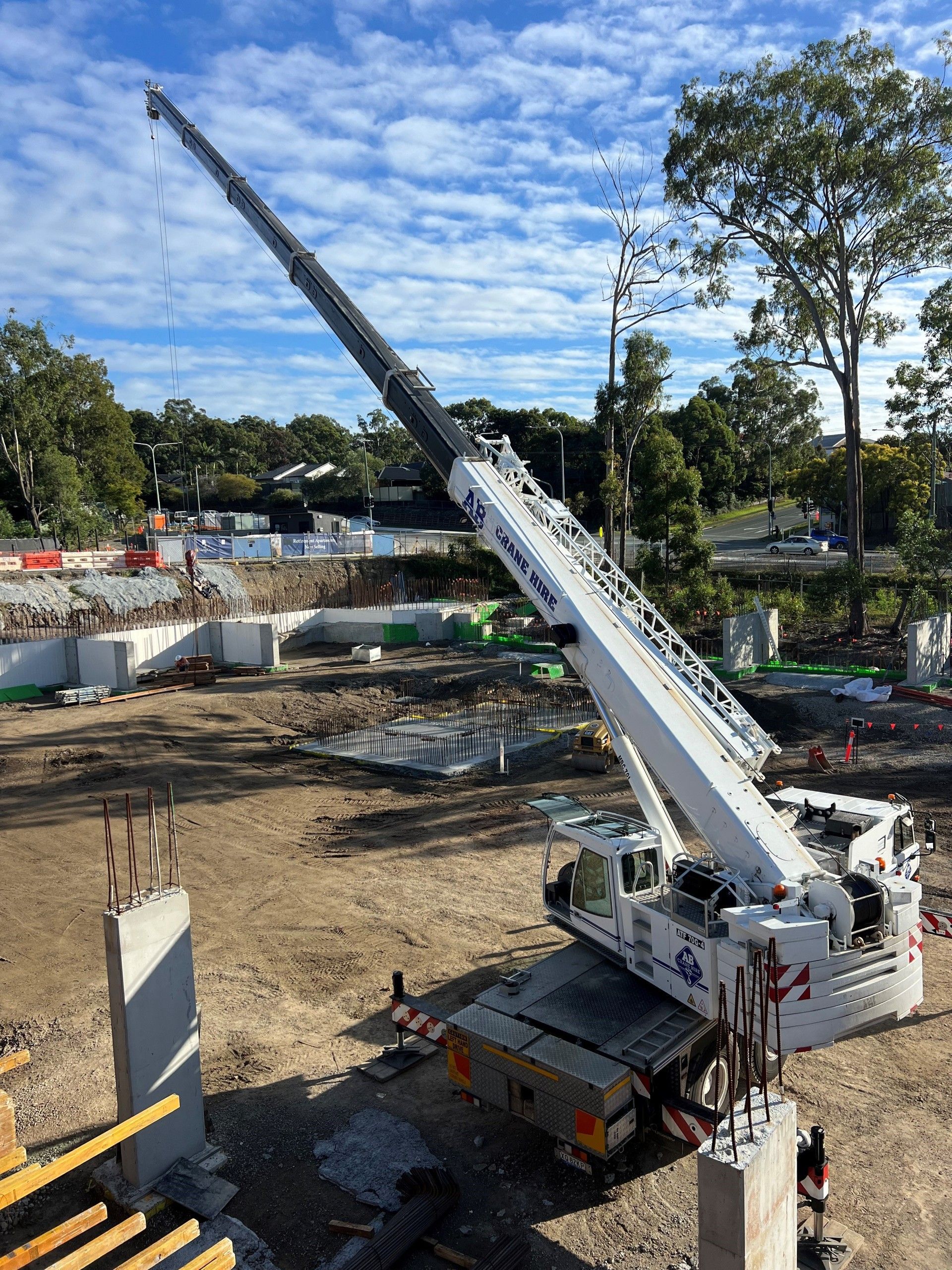 White crane truck at a construction site with its boom extended high over a dirt foundation.