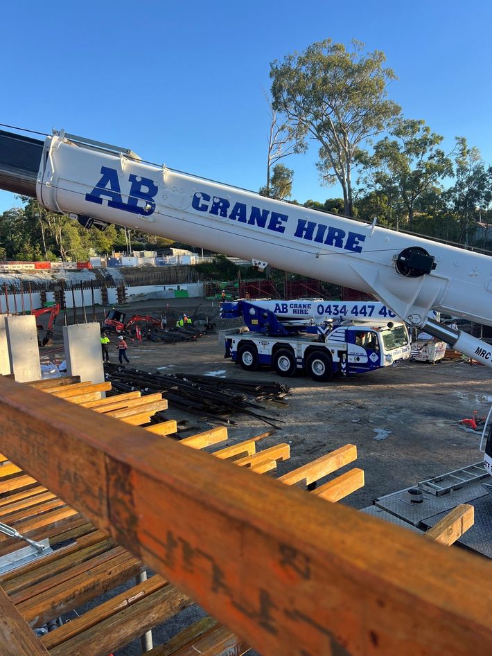 White crane truck labeled “AB Crane Hire” on a construction site under a blue sky