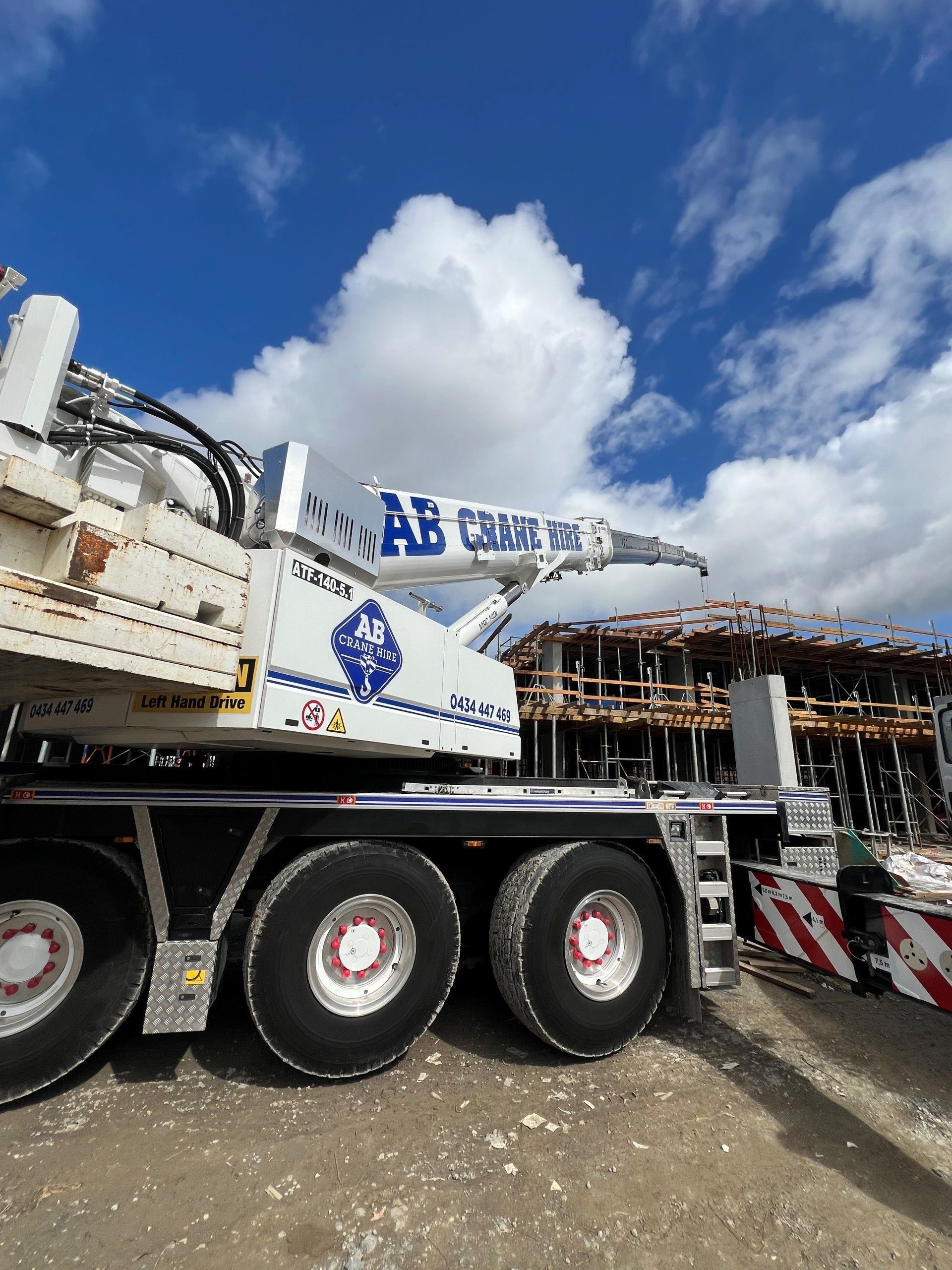 Large white crane truck on a construction site under a blue sky with clouds