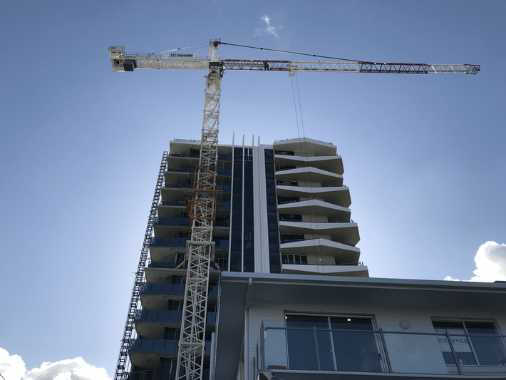 High-rise building under construction with a tower crane against a blue sky