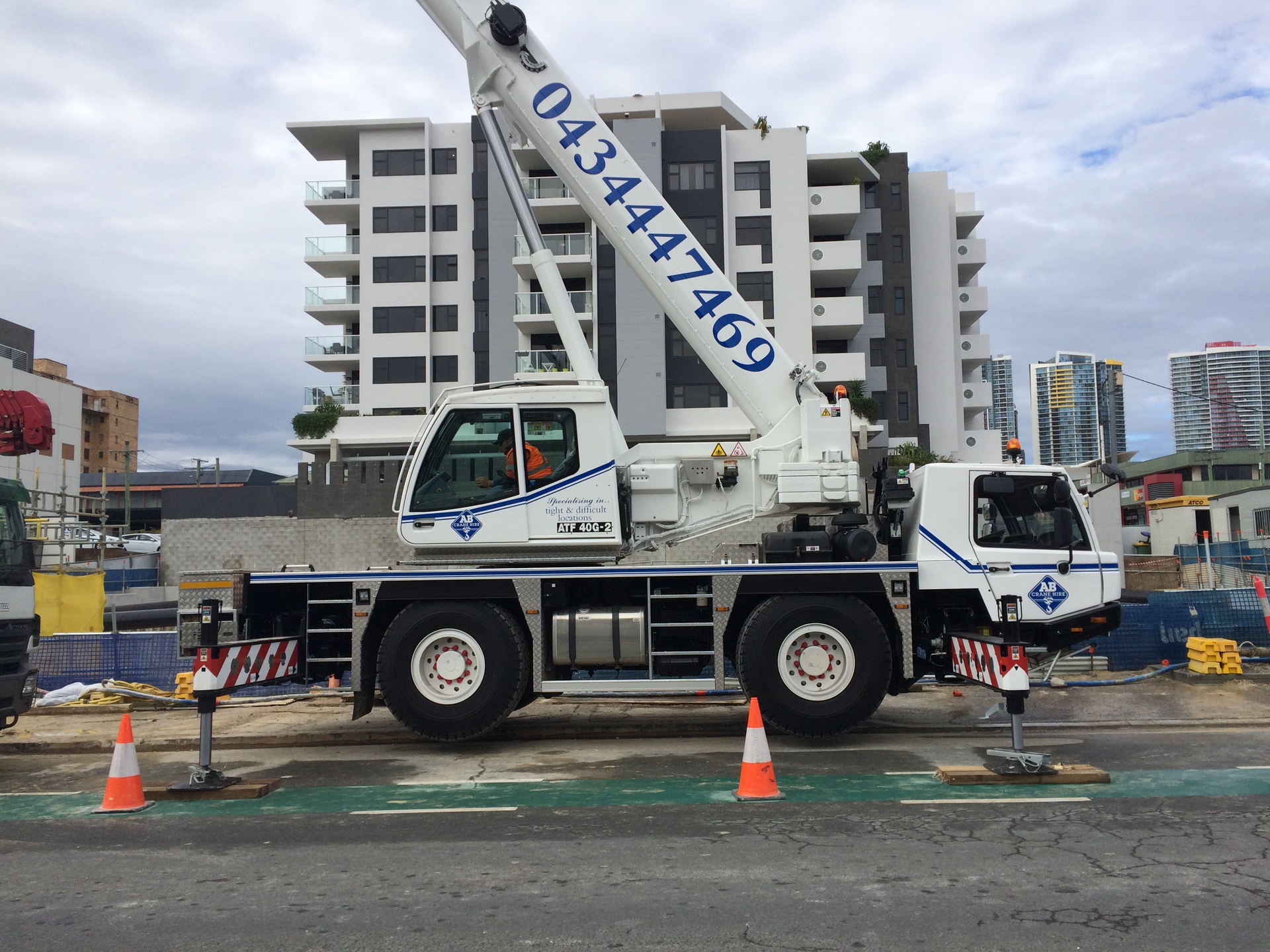 White crane truck at a construction site with apartment buildings in the background.