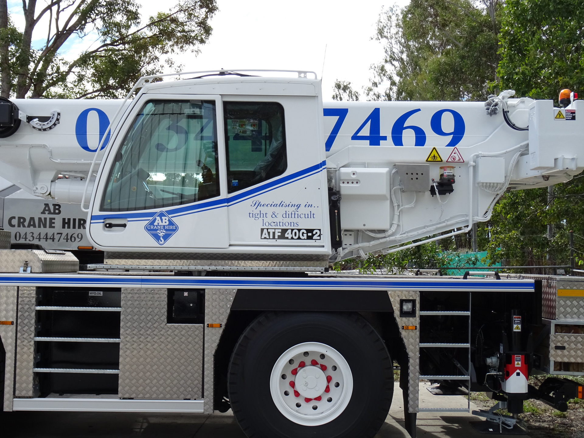 White utility crane truck with blue stripes and number 7469, parked outdoors.