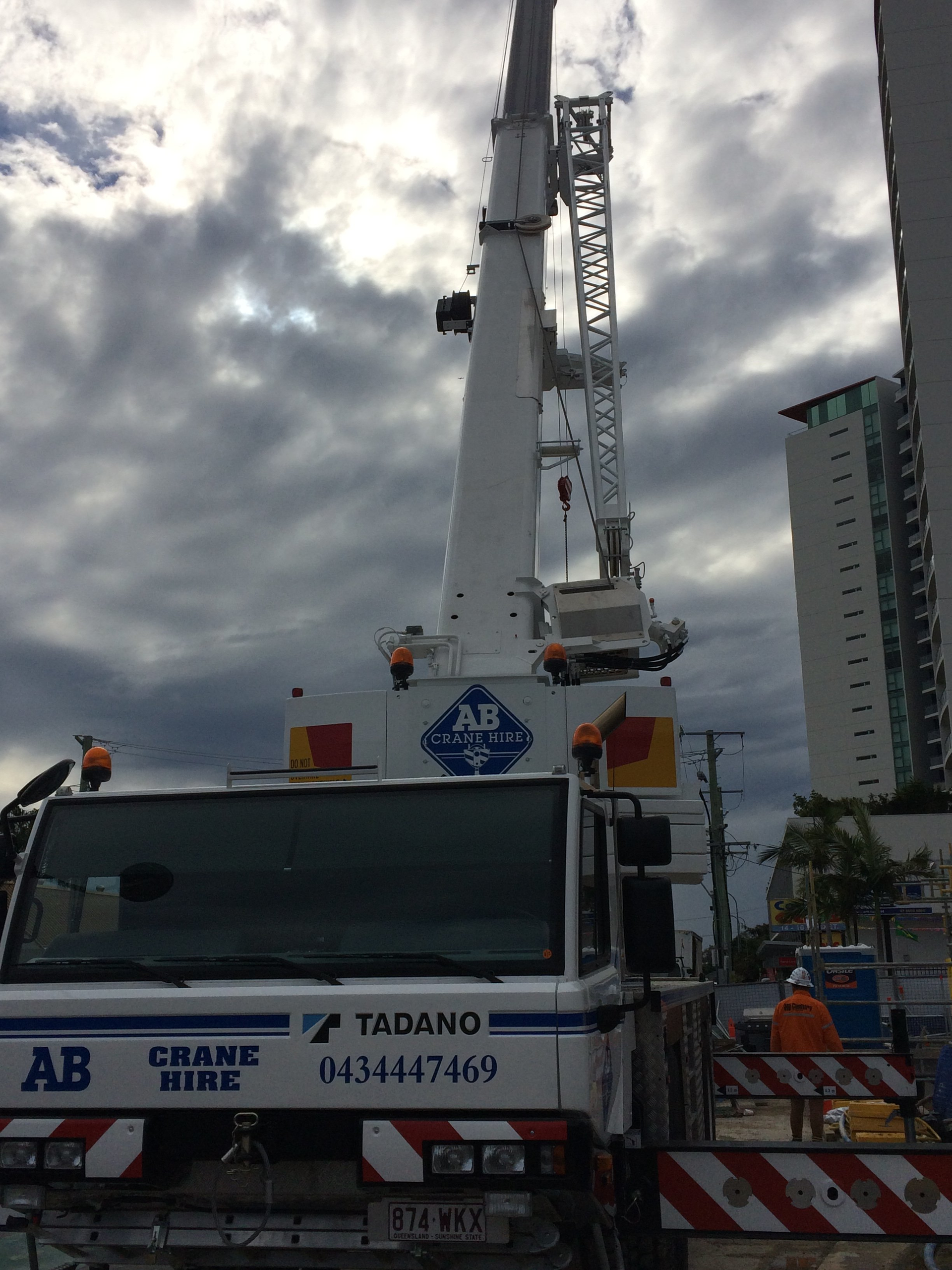 Mobile crane lifting equipment on a truck at a construction site under a cloudy sky