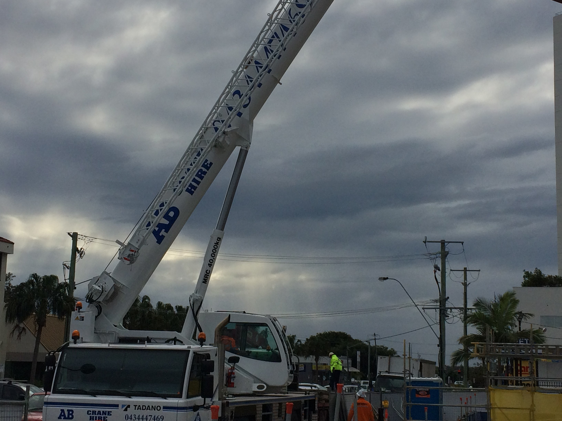 Tow truck with raised boom blocking a street under cloudy skies, with utility poles and traffic nearby