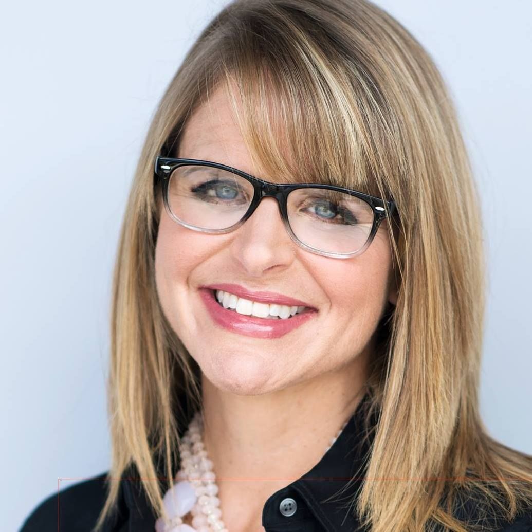Smiling person with blonde hair and black glasses against a light blue background