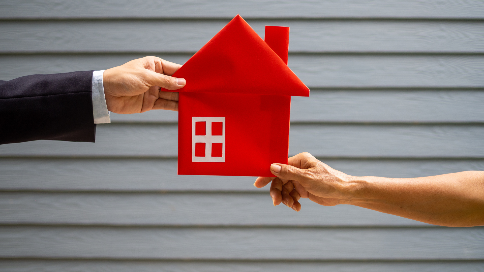 A man and a woman are holding a red house in their hands.