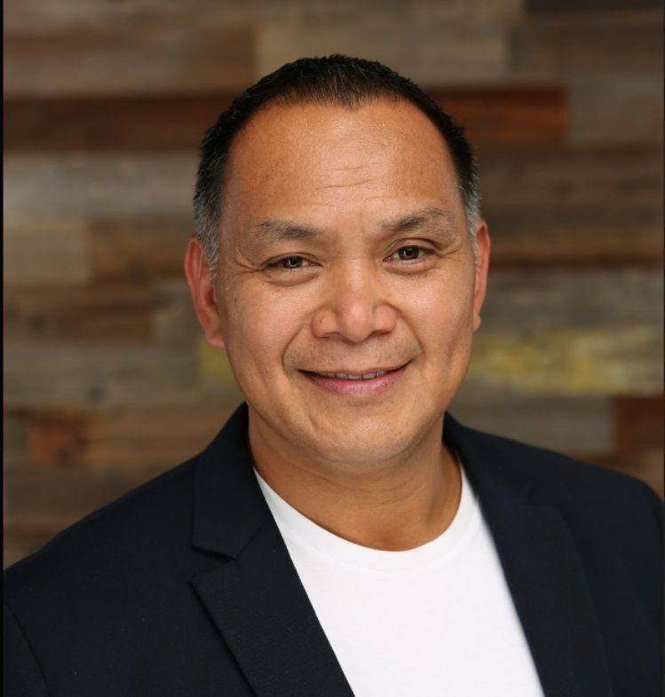Smiling man in a black blazer and white shirt against a blurred wooden background