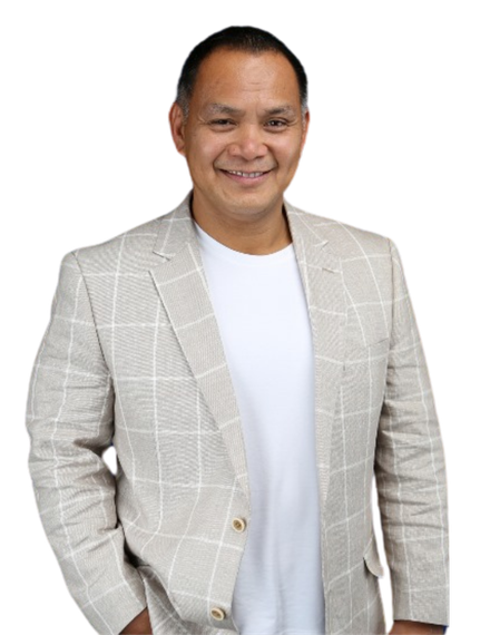 A man wearing a plaid jacket and a white shirt is standing with his hands in his pockets.