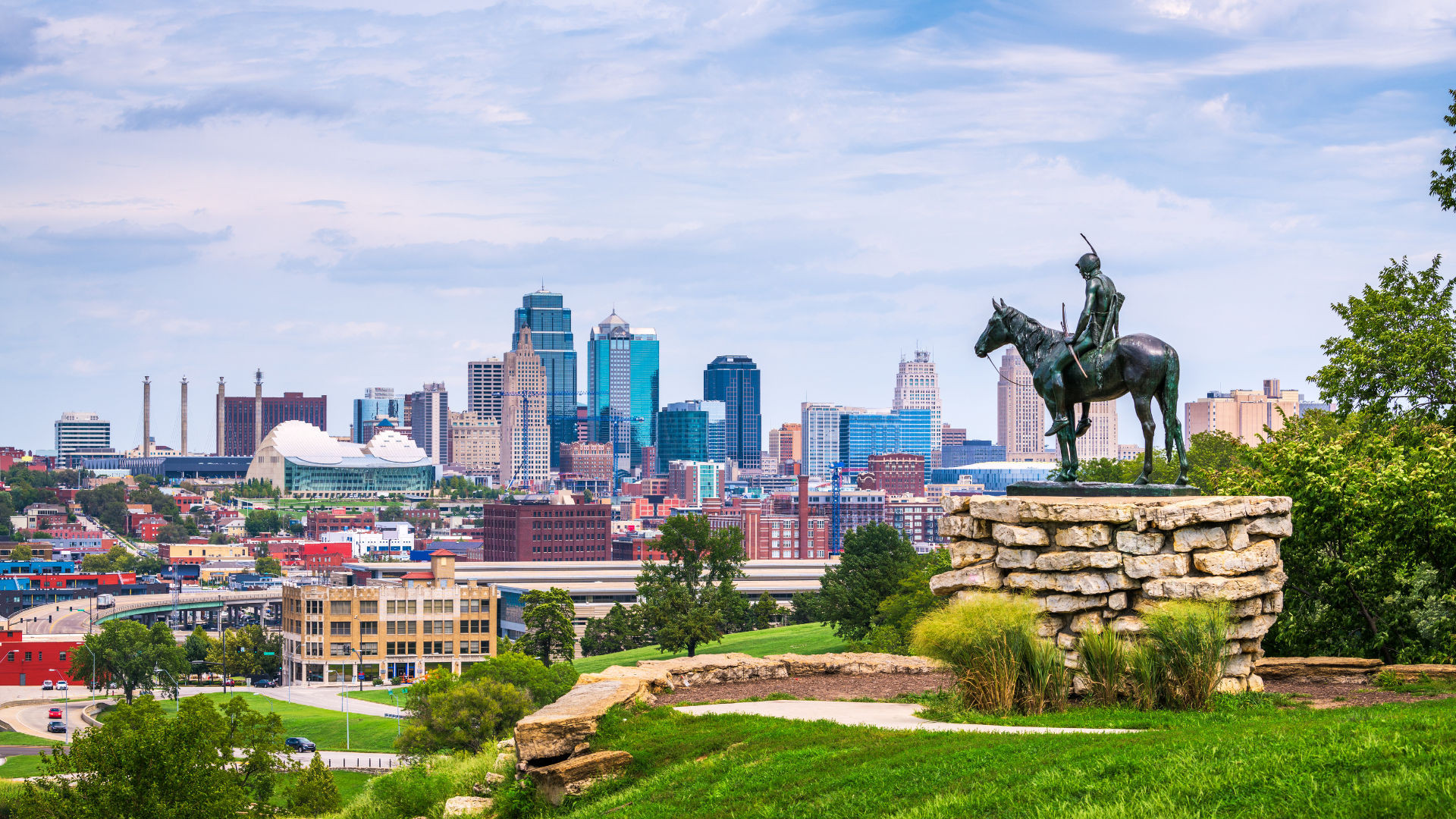 A statue of a man riding a horse in front of a city skyline.