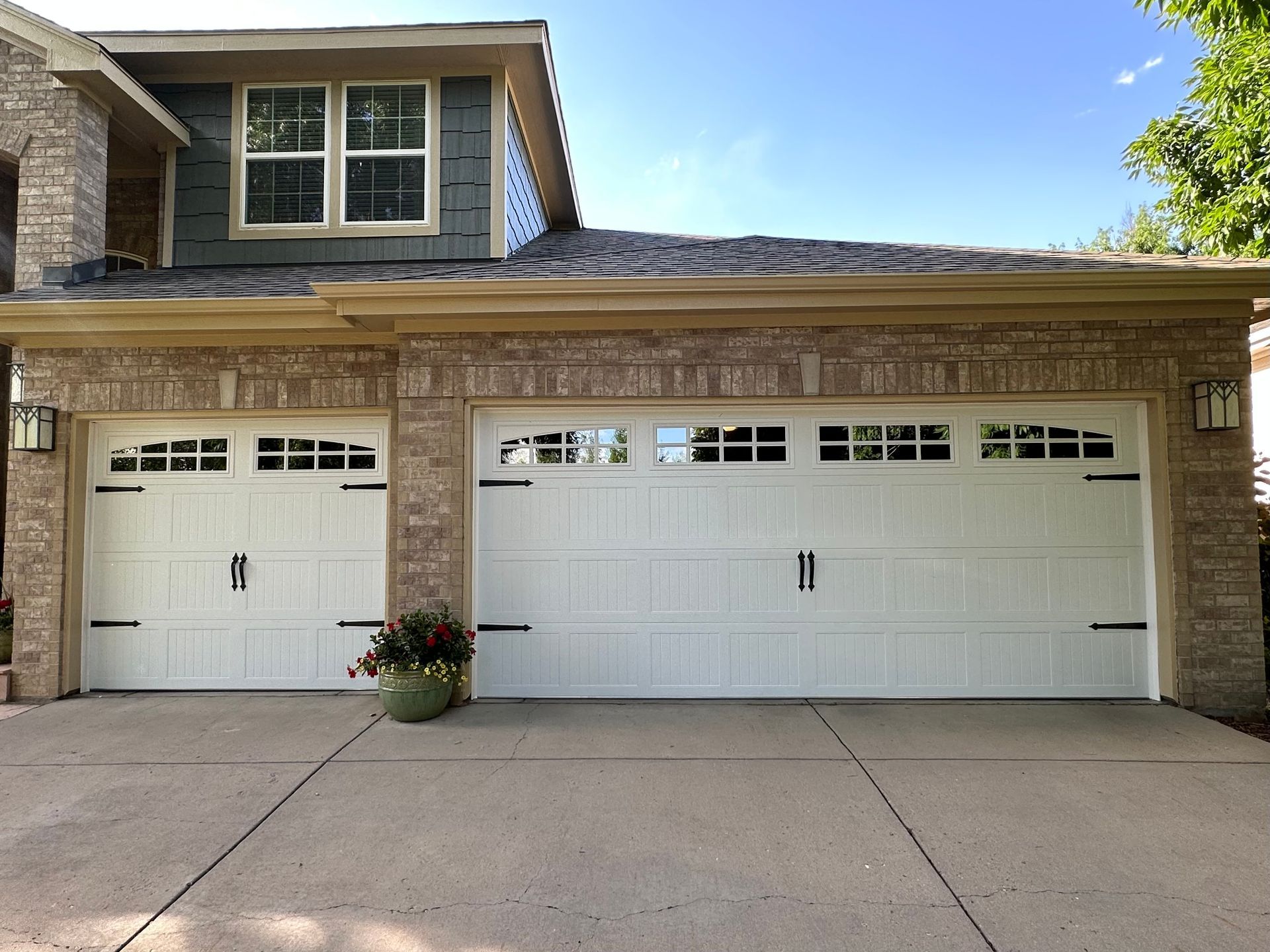 Two white garage doors with black accents, on a brick and stone house.
