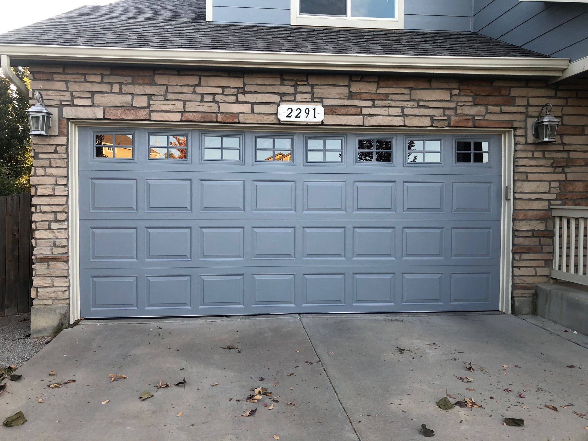Gray garage door with square panels and windows, set in a stone facade
