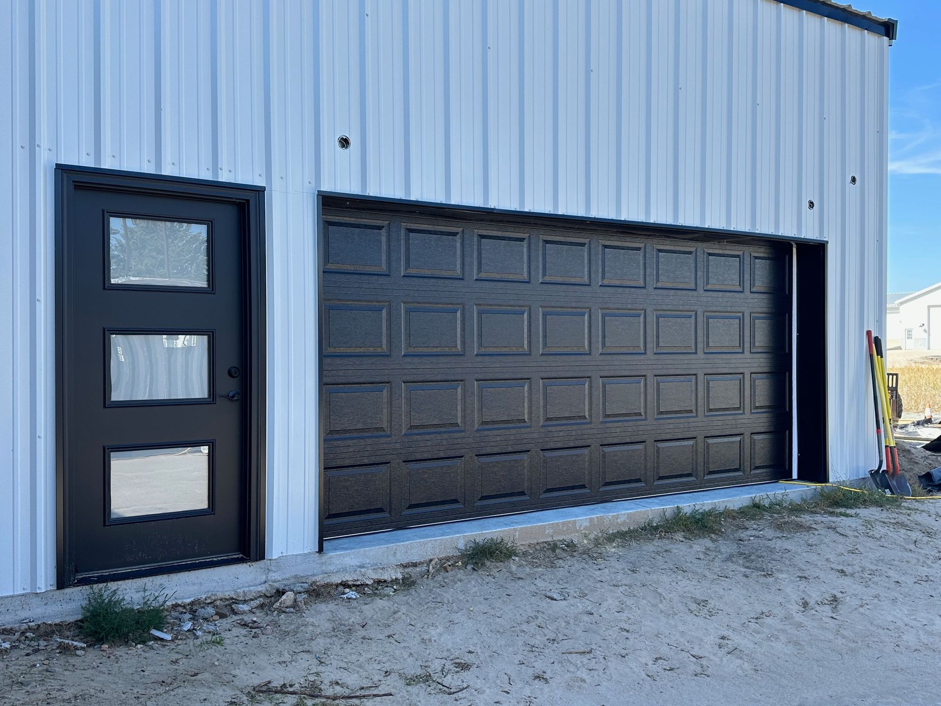 Black garage door and door with glass panes on a white metal building.
