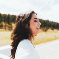 Testimonial woman smiling pleased outdoors evergreen trees in background