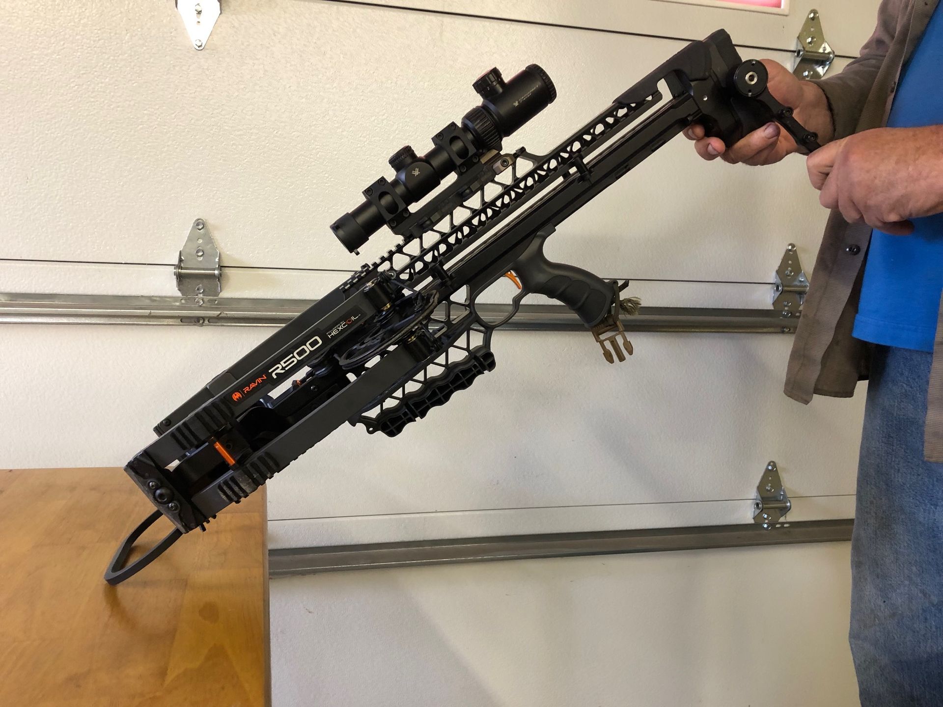 A man is holding a crossbow with a scope attached to it