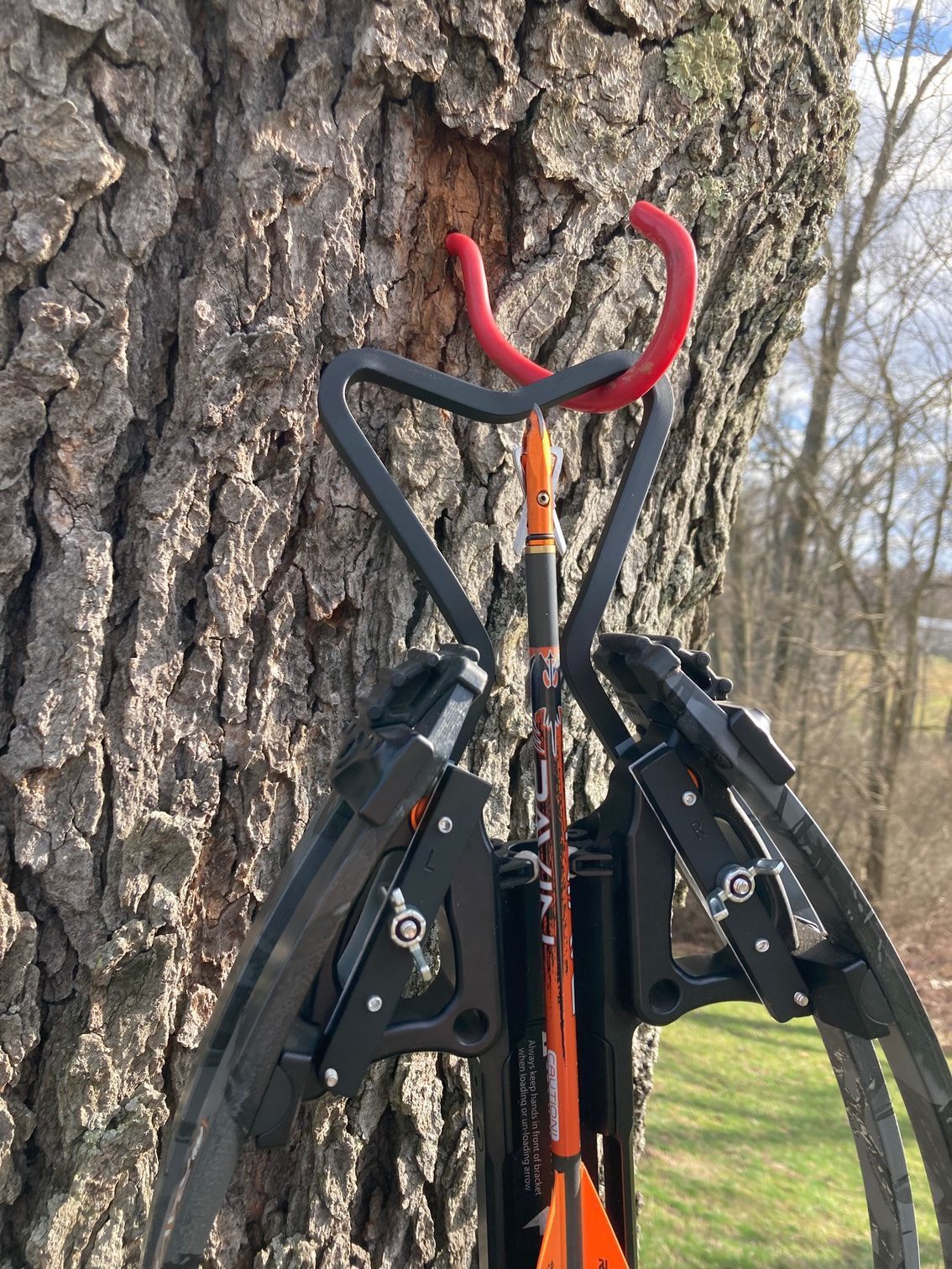 A crossbow is hanging from a hook on a tree.