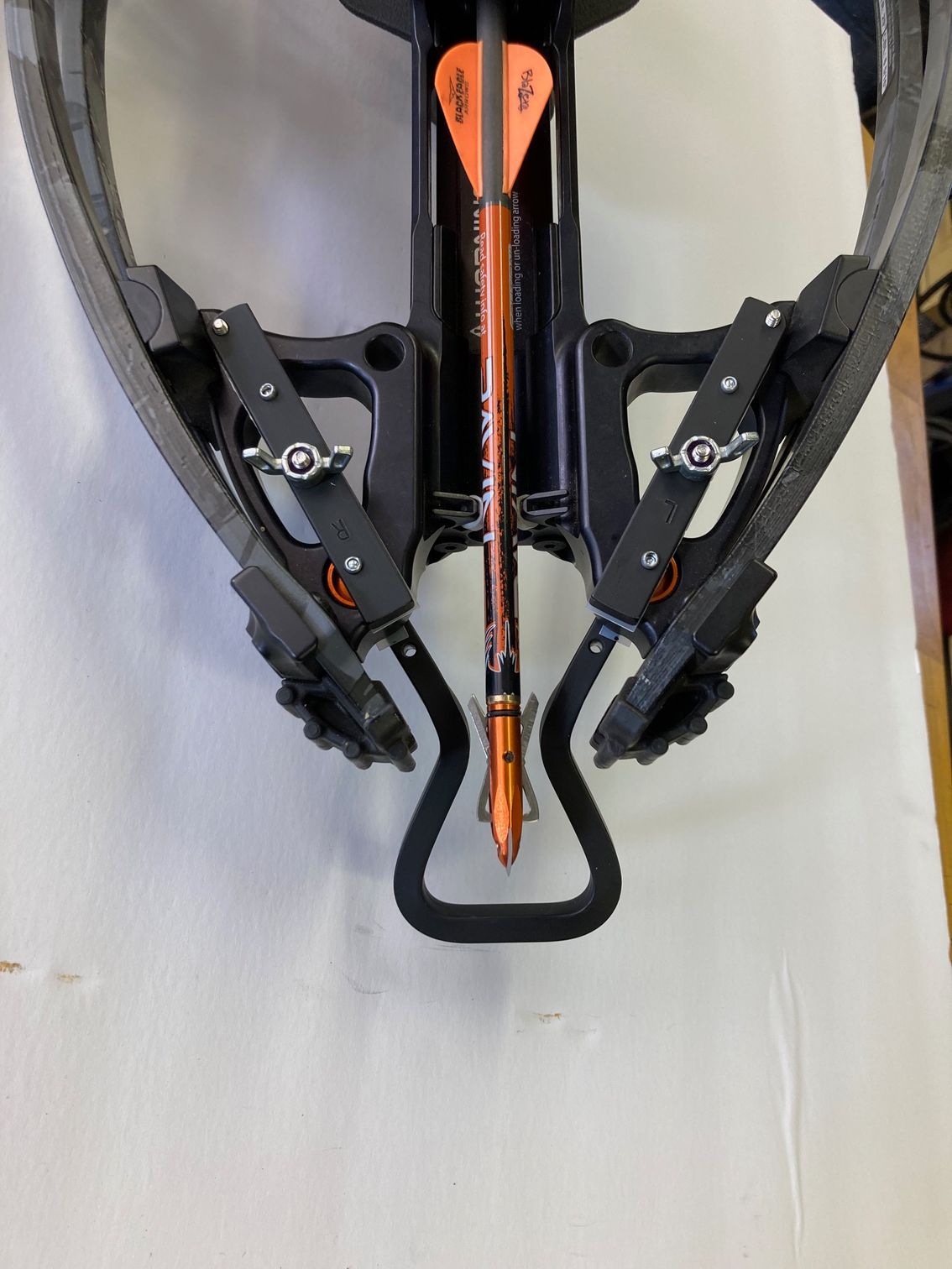 A close up of a crossbow with an orange arrow in it