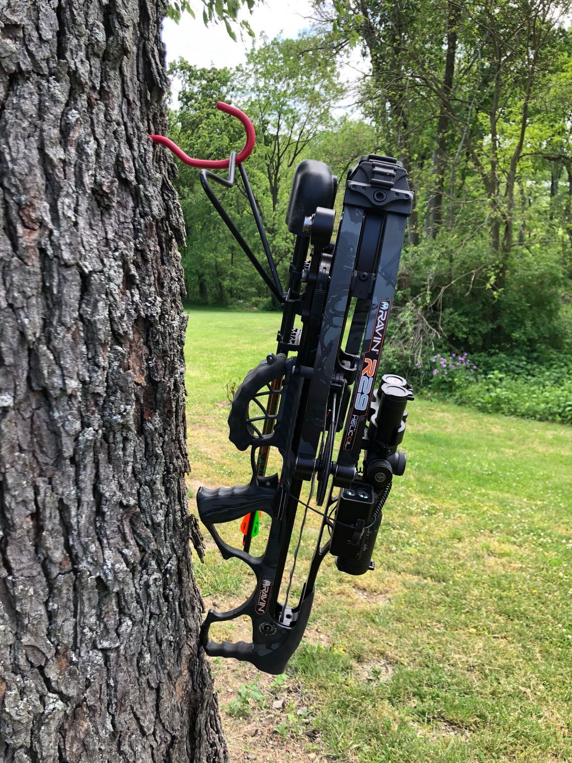 A Ravin Crossbow with 4N1 Lite Bipod attached, hanging securely to a hook in a tree. 