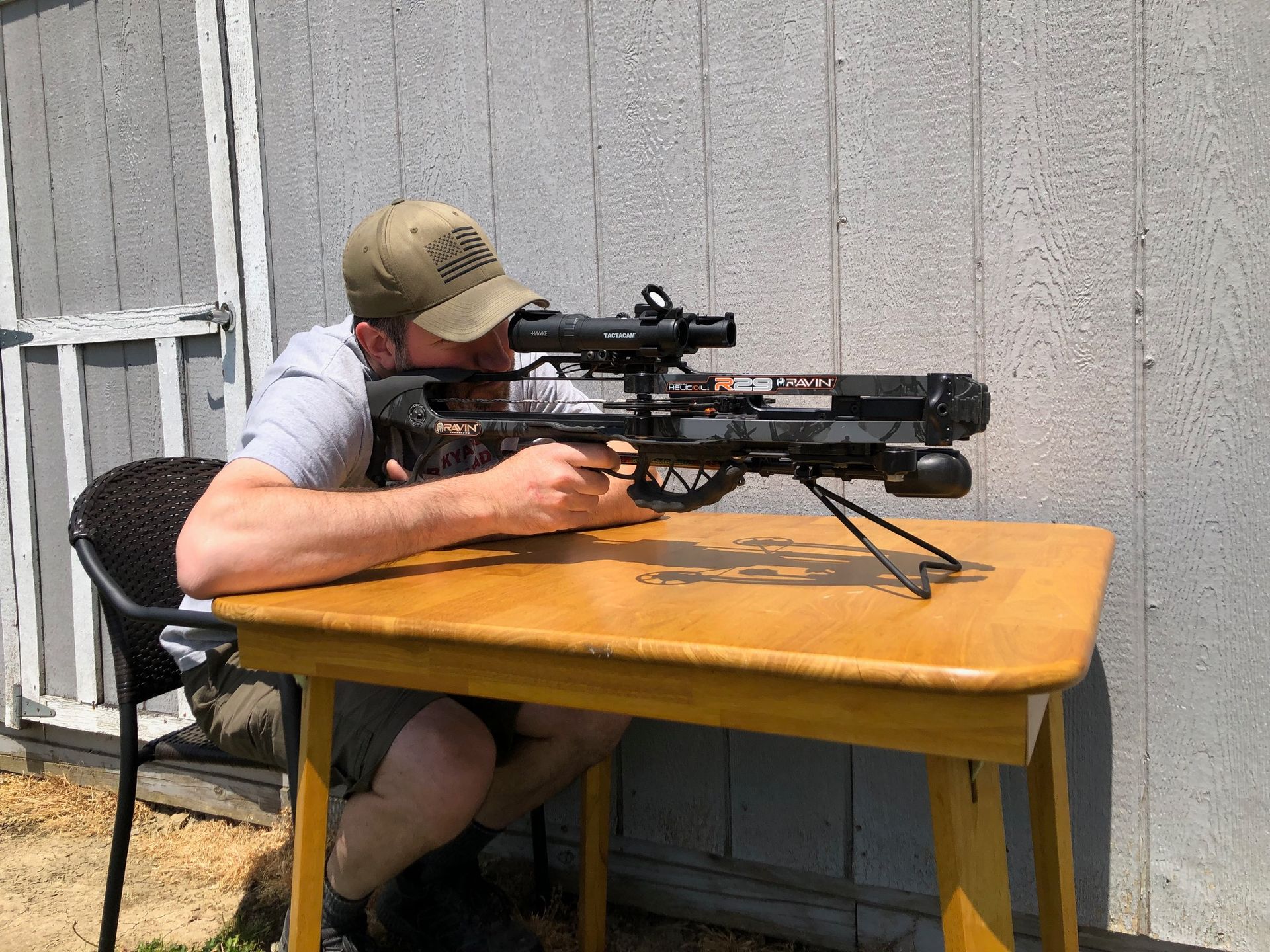 A man is sitting at a table holding a crossbow with the Bipod 4N1 Lite attached. 