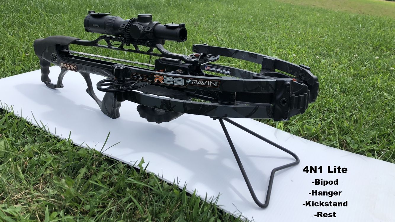 A crossbow is sitting on top of a white mat in the grass with 4N1 Lite bipod attached. 