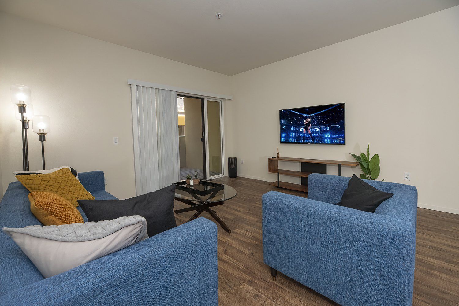 Luxury Apartments in El Cerrito, CA - Metro 510 - Living Room with Hardwood-Style Flooring, Sofa, Armchair, Coffee Table, Wall-Mounted TV, and Access to Private Balcony Through Sliding Glass Doors.