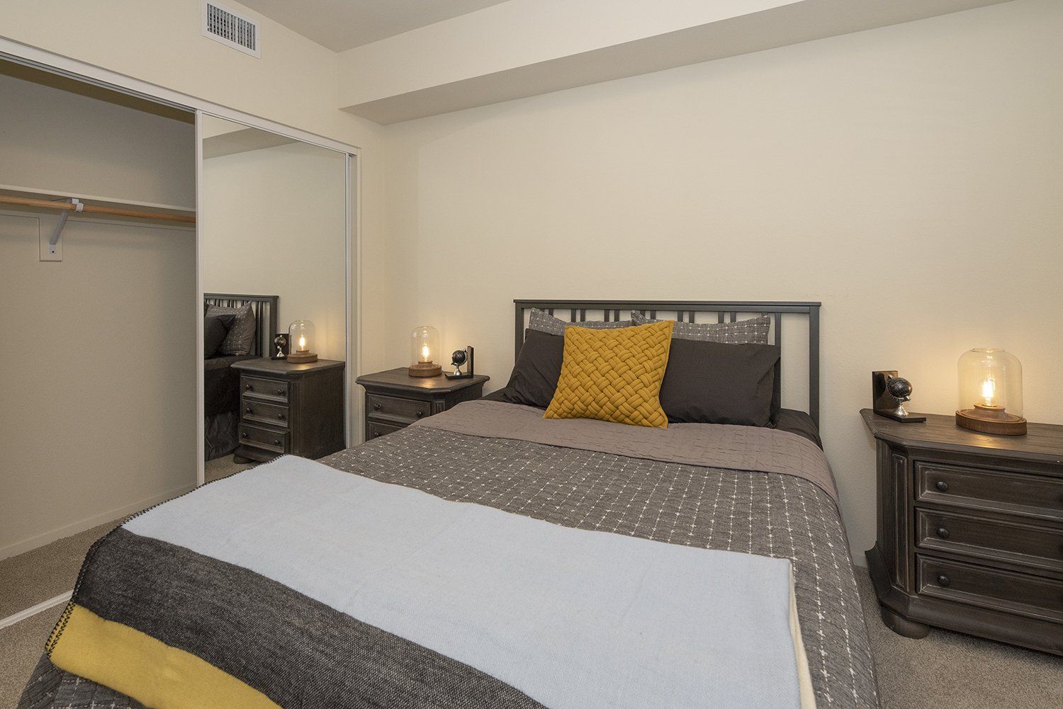 Apartments for Rent in El Cerrito, CA - Metro 510 - Bedroom with Carpeted Flooring, Bed, Nightstands, and Sliding Mirrored Closet Door.